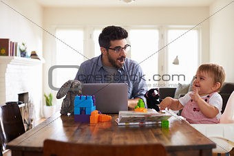 Father Works On Laptop As Baby Son Plays With Toys