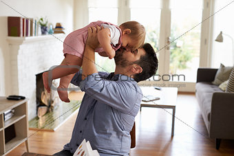 Father Sits At Table And Plays With Baby Son At Home