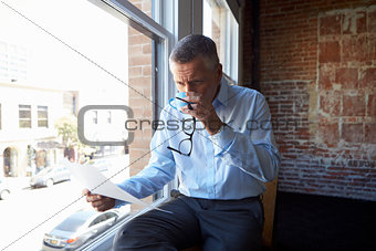 Businessman Reading Document Sitting By Office Window