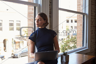 Businesswoman Sitting By Window Working On Laptop