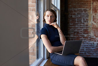 Businesswoman Sitting By Window Working On Laptop