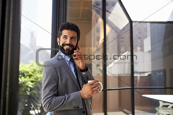 Middle aged Hispanic businessman using phone and holding cup
