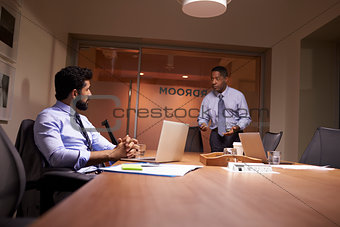 Businessman stands talking to work colleague late in office