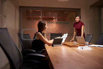 Businesswoman stands talking to colleague working late