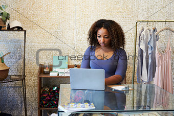 Woman working in clothes shop using laptop, front view