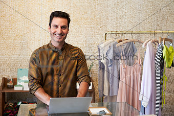 Young man working in clothes shop using laptop at counter