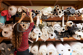 Young woman reaching to select fabric from storage shelves