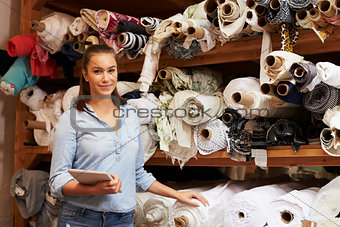 Woman using tablet in fabric storage warehouse, portrait