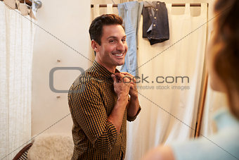 Woman watches her partner trying on shirt in changing room