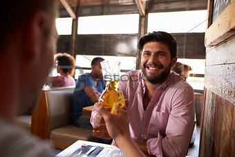 Two male friends in a bar making a toast with beer bottles