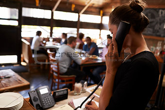 Young woman taking a reservation by phone at a restaurant