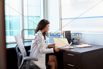 Female Doctor Wearing White Coat Reading Notes In Office