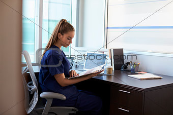 Nurse Wearing Scrubs Working At Desk In Office