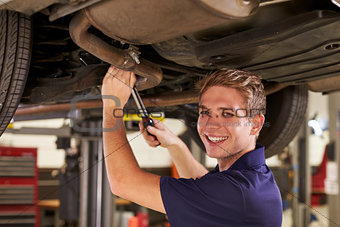 Portrait Of Auto Mechanic Working Underneath Car In Garage