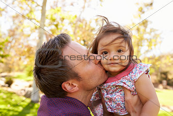 Father holding and kissing his young daughter in a park