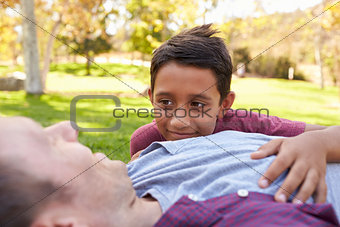 Mixed race boy lying in park with his white father, close up