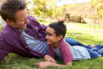 Mixed race Asian boy lying in a park with his white father