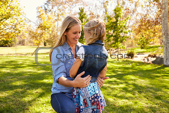Mother and daughter embracing in park, three quarter length