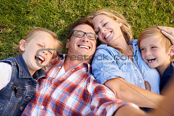 White family lies on grass taking selfie, camera out of shot