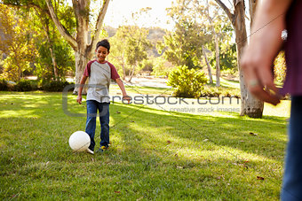 Seven year old boy playing football in a park with dad
