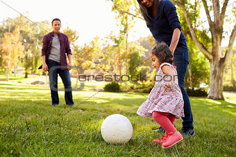 Parents kicking a ball with their young daughter in a park