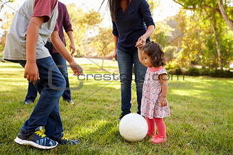Young mixed race family playing with ball in a park, crop
