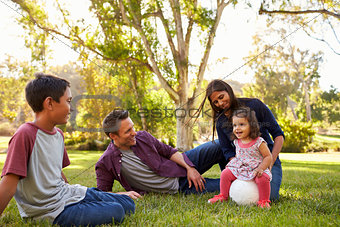 Young mixed race family relaxing with soccer ball in a park