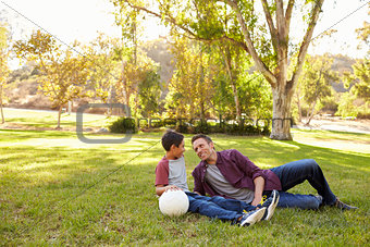 Father and son relaxing with soccer ball in a park