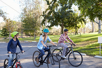 Parents and young son cycling together through a park