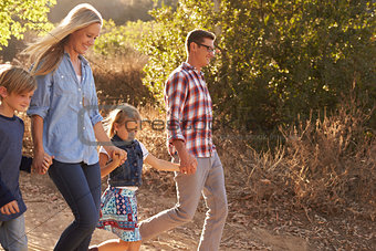 Young white family walking on a path in sunlight, side view