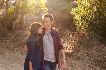 Mixed race couple walking in park embracing, waist up