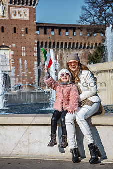 happy mother and daughter tourists in Milan, Italy rising flag