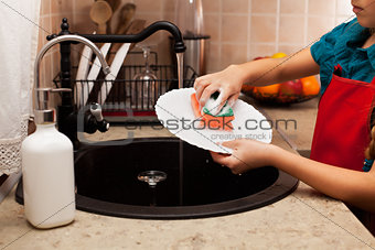 Child washing a plate with sponge at the kitchen sink, 