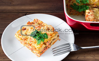 Close-up of a traditional lasagna topped with parskey leafs served on a white plate with fork