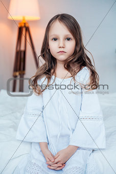 Cute little girl wearing nightgown sitting on the bed.