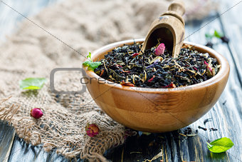 Dry black tea with flower petals in a wooden bowl.