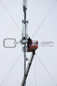 Two workers assemble equipment for telecommunications on the tower with the help of the lift in the winter