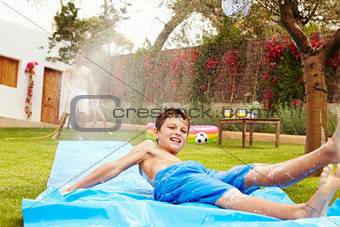 Father And Son Having Fun On Water Slide In Garden