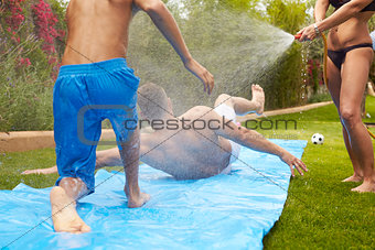 Rear View Of Family Having Fun On Water Slide In Garden