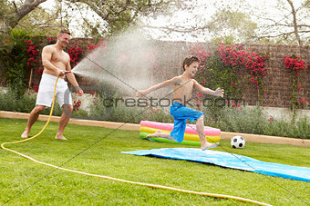 Father Spraying Son With Garden Hose