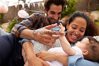 Family With Baby Playing On Rug In Garden Together