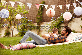 Father With Baby Relaxing On Rug In Garden Together