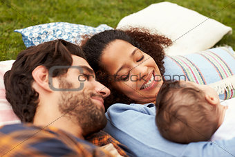 Family With Baby Relaxing On Rug In Garden Together