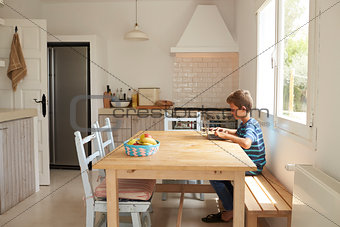 Boy At Home Using Laptop On Kitchen Table
