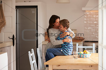 Son Sitting On Kitchen Table And Hugging Mother