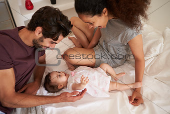 Parents Playing With Baby Daughter In Bedroom At Home