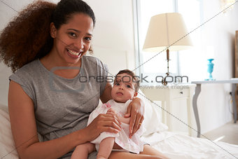 Mother Cuddling Baby Daughter In Bedroom At Home