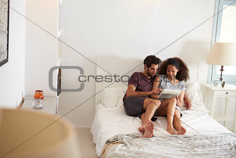 Couple Sitting On Bed Looking At Digital Tablet Together