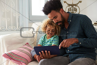 Father And Son Sitting On Sofa Using Digital Tablet