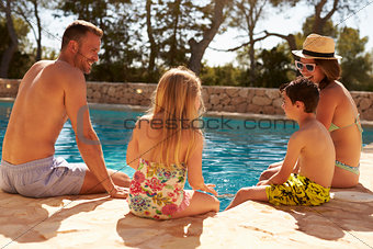 Rear View Of Family On Vacation Relaxing By Outdoor Pool